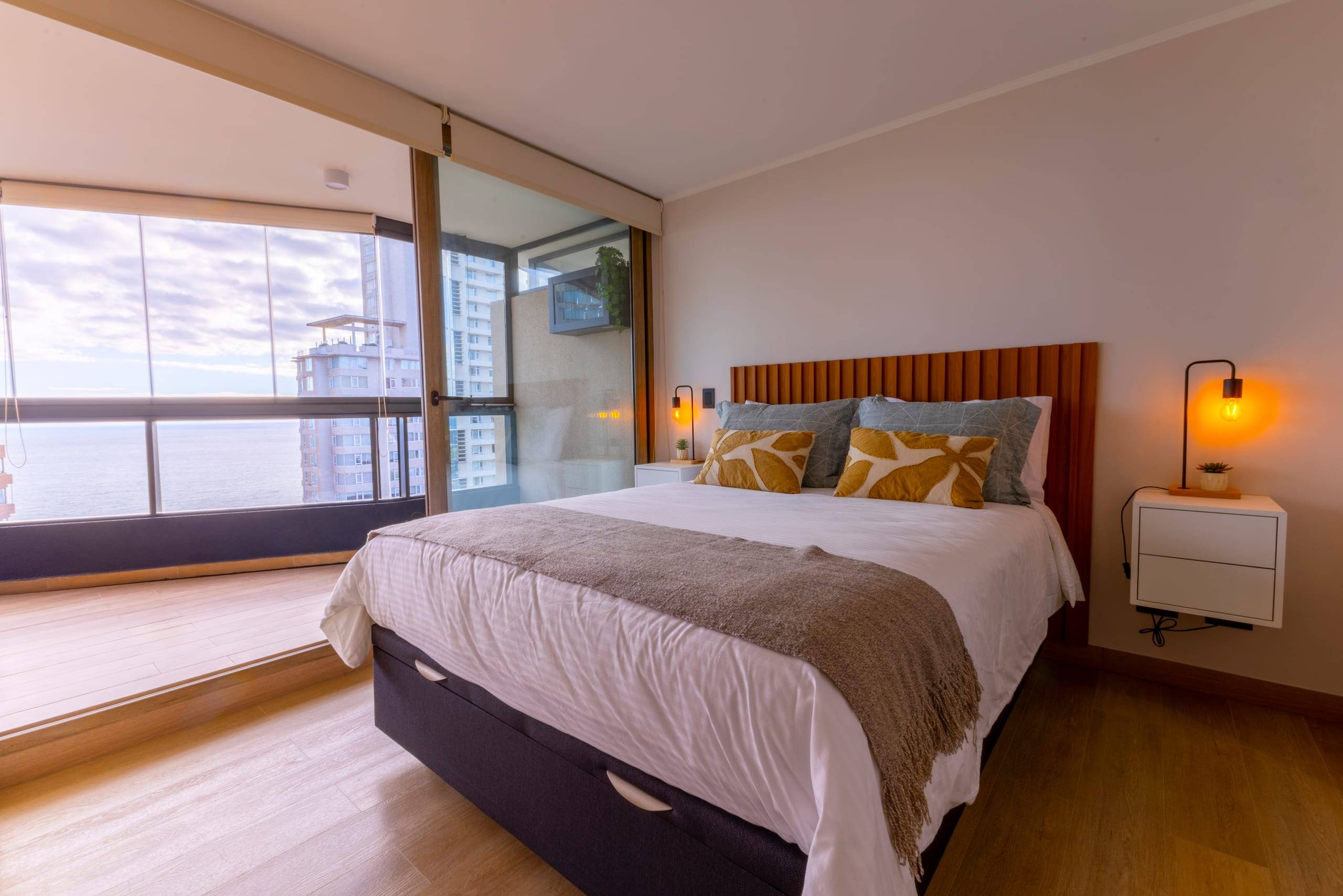 Dormitorio principal con respaldo de madera y ventanal con vista al mar en Concón